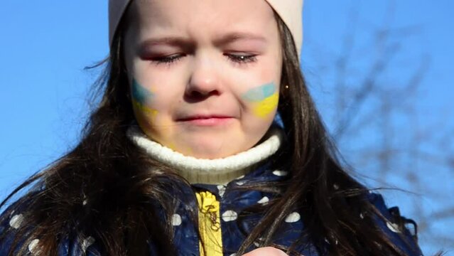 Little girl in tears because of the war. The girl is crying because of the war. War in Ukraine. The heart is painted in the color of the Ukrainian flag. Russian aggression against Ukraine.
