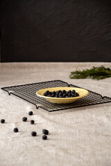 There is plate with fresh blueberries on metal stand. Berries are scattered nearby. Space for text. Selective focus. Image for articles about food.