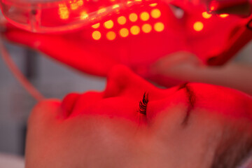 LED light anti-aging mask for facial skin care in a spa slow motion. A woman lies on a couch in a...