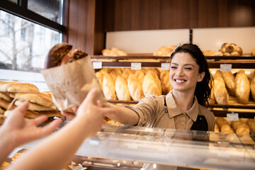 Working in bakery shop and selling fresh tasty pastry to the customer. - obrazy, fototapety, plakaty