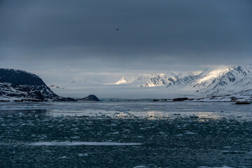 Fototapeta na wymiar Snowy mountains with peaks in the clouds. In Svalbard, Norway. Global Warming.