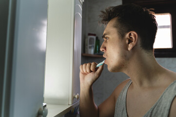 A young man is brushing his teeth in the bathroom during the day