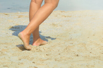 Women's feet on a sandy beach against the backdrop of the sea.