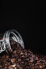 Coffee beans in a glass jar on a black background, close-up, selective focus, vertical frame. Roasting and preparing coffee, vertical frame