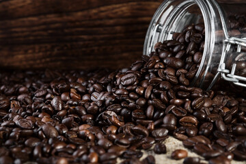 Fragrant coffee beans are scattered from a jar on a rustic tabletop background. Close-up, selective focus. Copy space banner.