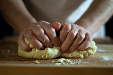Baker's hands working the flour dough on a wooden board