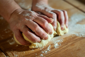 Baker's hands working the flour dough on a wooden board