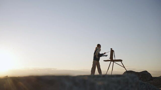 Full length shot of unrecognizable female painter creating picture outdoor, painting nature view in evening, empty space