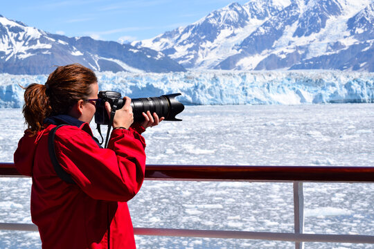 Happy female tourist takes photos from cruise ship deck as it sails close to the Hubbard Glacier in Alaska USA , capturing the image of the glacier before it is affected by global warming and climate 