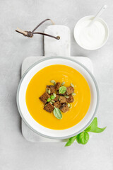Seasonal autumn roasted pumpkin and carrot soup with cream and rye bread croutons on a light concrete background. Top view.
