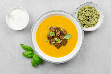 Seasonal autumn roasted pumpkin and carrot soup with cream and rye bread croutons on a light concrete background. Top view.