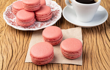 Berry macarons on a plate with coffee over wooden table