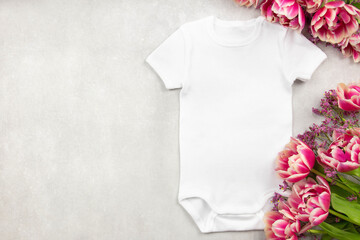 White baby girl or boy bodysuit mockup flat lay with tulip flowers on gray concrete background. Design onesie template, print presentation mock up. Top view. 