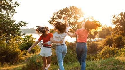 Group of girl friends jumping outdoors on sunset nature. Young multi-ethnic hipster friends dancing at summer party. Group of women friends hugging and ejoying the sunset in outdoor nature