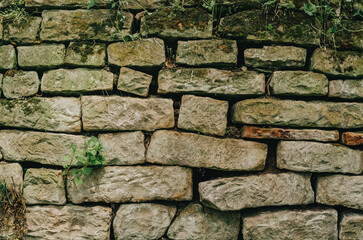 Old stone fence. Cracks between the stones. Moss on the ruined wall.