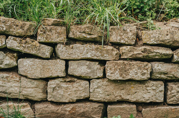 Fence of stone, overgrown with moss and grass. Stone texture. Aged architecture.