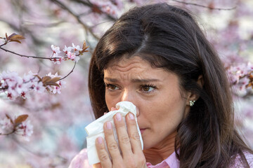 Girl wiping nose in front of blooming tree in spring