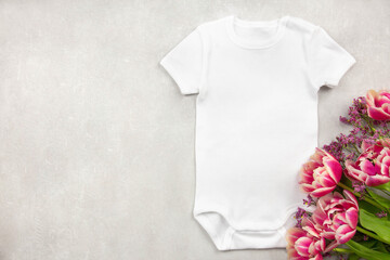 White baby girl or boy bodysuit mockup flat lay with tulip flowers on gray concrete background. Design onesie template, print presentation mock up. Top view. 