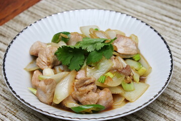 Stir-fried pork with chilli with onions and spring onions served in a white plate, Stir-fried pork with chilli is a popular Thai dish that Thai people eat.