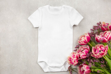 White baby girl or boy bodysuit mockup flat lay with tulip flowers on gray concrete background....