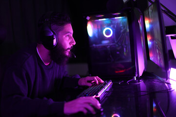 A gamer portrait of a young man determined to play video games on his computer wearing headphones in a dark room with colorful lights. © wanlaya
