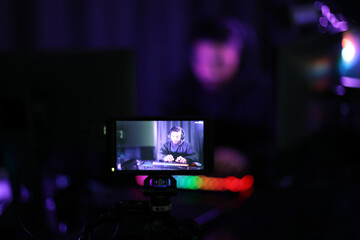 Fototapeta premium personal view photos through the screen Live show boys playing online games in headphones, keyboards are brightly colored. In a dark room with colorful neon lights