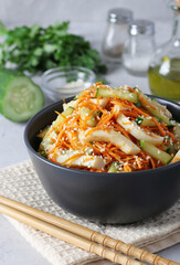 Salad with squid, carrots and cucumber, sprinkled with sesame seeds, in a dark bowl on light background