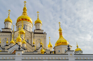 Fototapeta na wymiar Golden domes with crosses of the Orthodox Christian religious building against the cloudy sky. Pochaiv. Ukraine, 2022