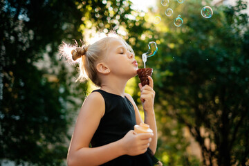 Child blowing soap bubbles. Girl is playing outdoors.