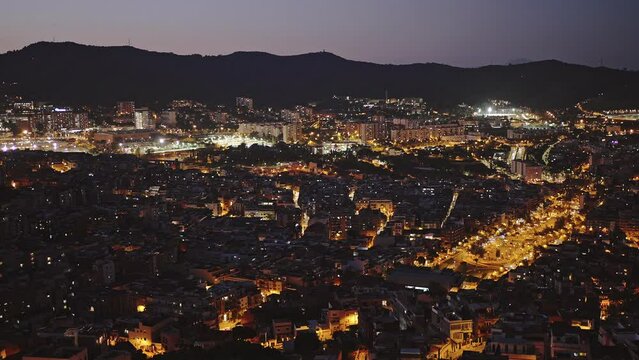 Panoramic view of night city glowing in doline, mountain silhouette over evening sky, empty space