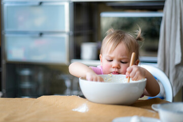 Little cute funny girl licking the dough from her finger helping mother prepare pie cake in...