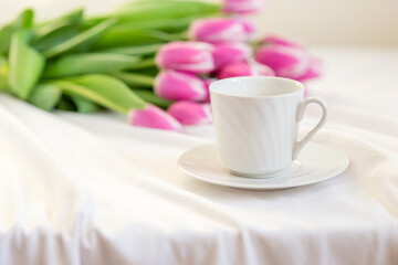 Fototapeta na wymiar Spring still life with a white mug with a saucer and a bouquet of beautiful pink tulips