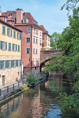 Fototapeta na wymiar Apartments reflect on the waters of a canal flowing through the city of Bamburg, Germany on a vivid summer day.