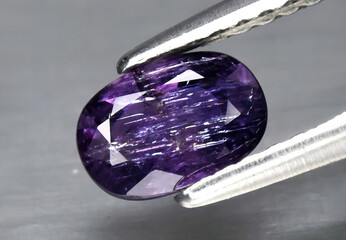 Natural gemstone purple sapphire in tweezers on a gray background