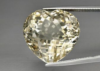 Natural gemstone yellow topaz in tweezers on a gray background