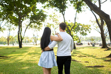 Fototapeta premium Back of multiracial couple walking in an urban park holding each other's backs