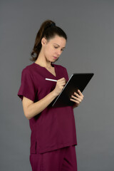 female doctor in purple uniform filling out report on digital tablet on gray background side