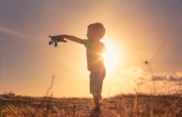 Little child playing with his toy airplane in a field at sunset 