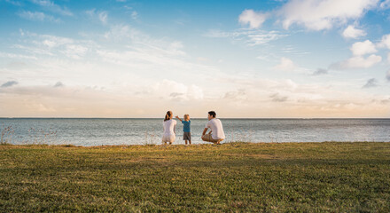 Mother, father, and child relaxing together by the sea at sunset 