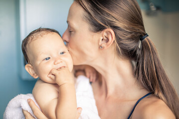 Mother kissing adorable baby girl after giving her bath 