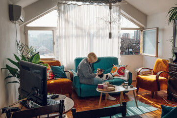 Woman cuddling and playing with her dog at home on the couch