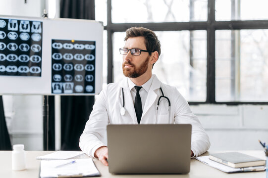 Medicine and health concept. Pensive caucasian general medicine doctor with glasses, therapist, pulmonologist, in medical uniform, sits at workplace in hospital, looks to the side , thinking