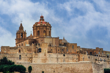 Fototapeta premium Mdina, Malta Silent City citadel with 12th century Metropolitan Roman Catholic Cathedral of Saint Paul - Il-Katidral Metropolitan ta San Pawl, against blue sky with clouds. 