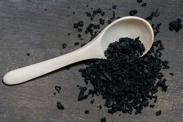 dry wakame seaweed in a jar on a white background on a wooden spoon lying on a dark cutting board