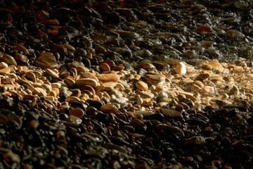 Obraz premium Sea pebbles. Small stones texture. A ray of sunshine in the surf of the sea.