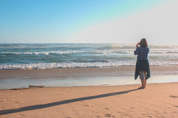 mujer joven con lentes disfrutando la playa, fotografiando y mirando el mar