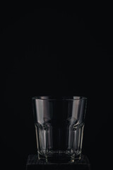 Empty glass for whiskey, brandy or bubon, old fashion type, copy space, selective focus on black background and wooden table.