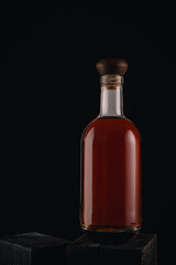 Glass bottle filled with brandy or whisky on black background. Bottle of alcoholic drink on wooden table.