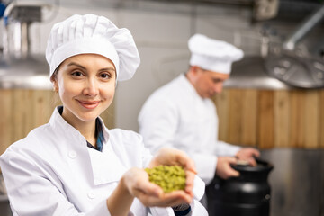 Smiling woman brewer holding bunch of hop pellets and looking at camera.