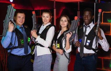 Group of adult co-workers holding laser guns and posing at laser tag room